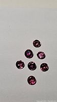 Seven small round hot pink purple sapphires on a light background, showing natural sparkle and color consistency.