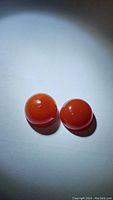 Two round cabochon red carnelian gemstones photographed on white surface showing smooth, shiny finish and deep orange-red color.