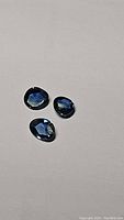 Three natural rose cut sapphires laid out on a plain light background, showing their multicolored blue tones and faceted rose cut style.