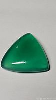 Close-up image of a polished trillion cut vivid green onyx gemstone showing smooth surface and bright color.