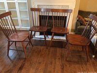 Four brown wood spindle-back chairs in a row on wooden floor showing overall shape and style