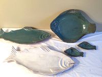 Five ceramic fish-shaped platters and items laid out on cloth, showing all pieces distinctly.