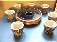 Seven small black and white ceramic pots arranged around a round wooden plant stand on a dark surface.