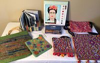 Overall lot showing paint kit, pencils, book, oven mitt, and four woven purses displayed on table.