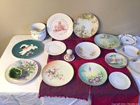 Assortment of vintage china laid out on table including plates, saucers, planter, and salt shaker holder altogether.