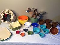 Wide view of colorful kitchen items including bowls, ceramic dishes, covered soup bowls, ceramic sauce bowls, bamboo steamer, and utensil pot.
