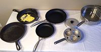 Full lot including the two cast iron skillets (one new Lodge and one vintage used), Danish Scanpan frying pans, vintage egg poacher, Cuisinart skillet with lid, and kitchen utensils