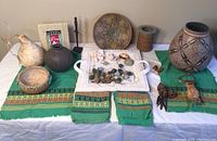 Full display of lot items on white surface with green textile base showing large pottery vase, spherical vase, gourds, white ceramic tray and wooden carved pieces.