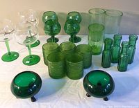 Full view of all green glassware items against a white cloth background showing variety of glasses, bottles, and candle holders