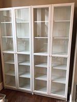 Four assembled white shelving cabinets with glass doors side by side