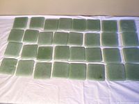32 four-inch square matte jade green ceramic tiles with one chipped tile spread on white cloth