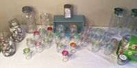 Wide view of most Mason jars and spice jars arranged on table with two large jars filled with sea shells and multiple colored lid jars near front