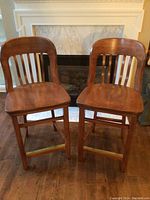 Two solid wood bar stools with brown finish seen from the front, showing seats and backrests with vertical slats.
