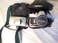 Minolta SRT 101 and Olympus Stylus quartz date cameras displayed with carrying cases, showing overall condition and included accessories.