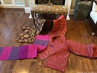 Piano bench with floral upholstery, four table runners laid out in front, and part of wicker basket visible beneath bench.
