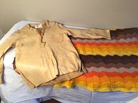 Vintage buckskin leather shirt laid out next to crocheted afghan showing color and pattern details.
