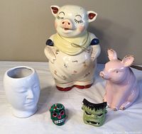 Image of all six ceramic items including pig cookie jar, pink pig figurine, white head vase, Frankenstein face, and colorful skull face.