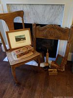 Oak chair with cane seat and various wood decor items including a framed print, small boxes, and carved wood headboard positioned in front of fireplace