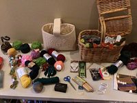 Whole lot showing yarn, baskets, woven bag, needles, scissors, and accessories on table.