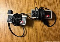 Two original Nintendo NES controllers with wires wrapped around them, shown on a wooden surface.