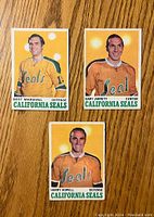 Front view of three 1970-71 O-Pee-Chee hockey cards showing California Seals players Bert Marshall, Gary Jarrett, and Harry Howell in orange jerseys.