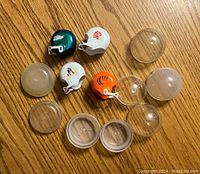 Four vintage NFL mini helmets with eight clear plastic display domes spread on table.