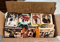 Cardboard box labeled 'Over 1500 Hockey Cards' filled with assorted hockey cards arranged in piles showing different player photos.