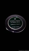 Close-up view of the front face of the round metal measuring tape. Features a green label with Atomic Energy of Canada Limited logo and text.