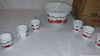 Set of six small cups arranged in a semicircle in front of the punch bowl on white cloth