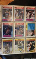 Nine cards displayed in a nine-pocket page: six Record Breaker cards at top two rows showing players breaking records; three Boston Bruins base cards in bottom row (Ray Bourque #7, Wayne Cashman #4, Bruce Crowder #36)