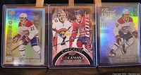 Front view of three Cole Caufield hockey cards in protective sleeves showing holographic and foil design elements.