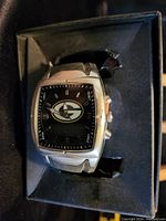 Silver-tone men's watch with rectangular black dial and Green Bay Packers logo on face, displayed in original packaging, showing buttons on side and black strap.