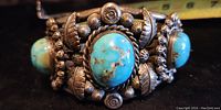 Close-up view of the center of the bracelet showing a large oval turquoise stone set in detailed silver bezel with leaf and granulation decoration.