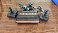 Atari Flashback 2 console with two connected joystick controllers, power adapter, and video cable on a wooden surface