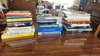 Stack of various coffee table and non-fiction books including art books and manuals on a wood surface.