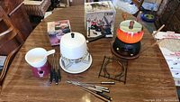 Full lot of fondue sets on dining table showing both enamel fondue pots with stands, burners, and forks.