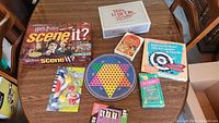 Overview photo showing all games and accessories spread out on a wood table including Harry Potter Scene It, Win Lose or Draw, Mille Bornes, Outburst, Chinese Checkers, and others.