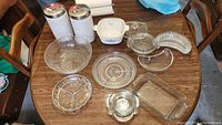 Overall lot showing white stoneware canisters, CorningWare casserole dish with 2 lids, and various clear glass serving and baking dishes on a wooden table.