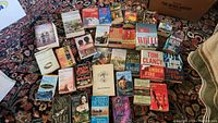 Top down photo of 32 assorted novels laid out on a carpet, titles and authors visible including John Grisham, Tom Clancy, Jackie Collins, Ken Follett, Nora Roberts, Stephen Frey, David Gemmell, Tom Wolfe, and John Jakes.