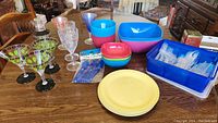 Overview of the full set of plastic dishes, bowls, utensils, wine glasses, and martini glasses on a wooden table