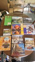 Photo showing the assortment of 10 puzzle boxes laid out on a table. Various scenic and illustrated cover art visible including a teddy bear, hot air balloons, countryside, and boats.
