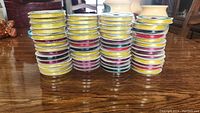 Front-facing image showing rows of ribbon spools stacked on a table with various satin ribbon colors, mainly yellow, red, black, and pink.