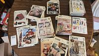 View of assorted sewing pattern packets spread on a table showing various doll clothing, decor, and craft patterns.