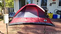 Front angled view of 4 person dome tent on wooden deck, showing red and gray panels.