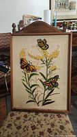 Front view of the framed hand embroidered wall art showing three Monarch butterflies and yellow flowers on a beige fabric background in a wooden frame.