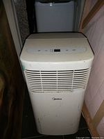 Front view of a white Midea portable air conditioner with control buttons and display on top, showing some signs of use and dirt marks.