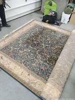 Photo of the partially unrolled Persian style area rug showing the dark floral patterned front and beige border.