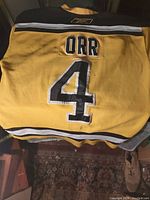 Back of vintage hockey jersey showing 'ORR' name and number 4 in black and white on yellow fabric with black and white stripes