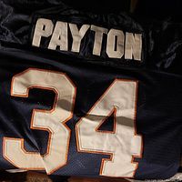 Back of vintage sports jersey with 'PAYTON' and large number '34' in white with orange trim on navy blue fabric.