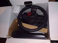 Gaming steering wheel, pedals, and shifter inside open box taken from above.